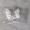 A clear plastic bag contains two white, ruffled collectible figurines.