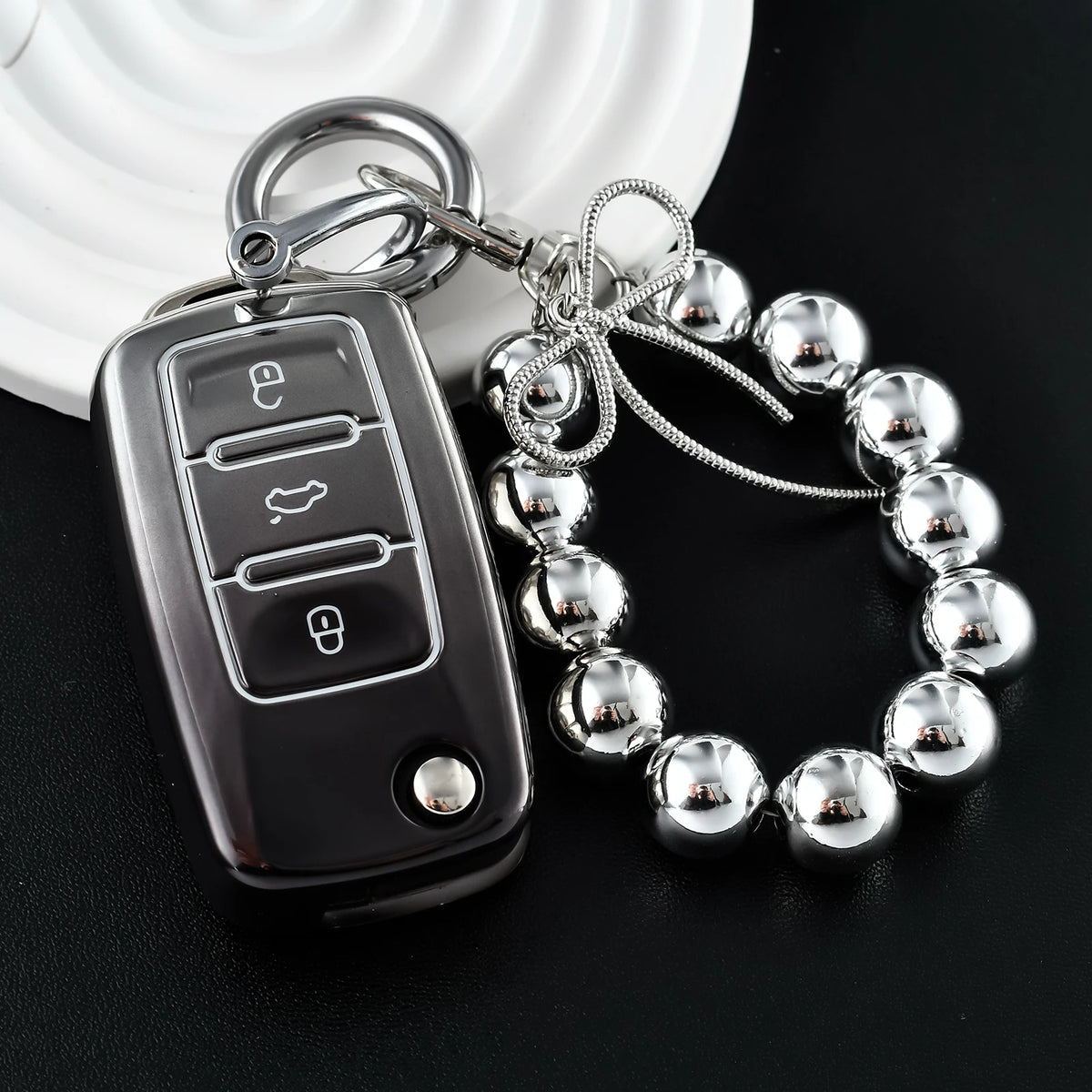 A silver car key fob attached to a chain and a bracelet of chrome-plated metal balls.
