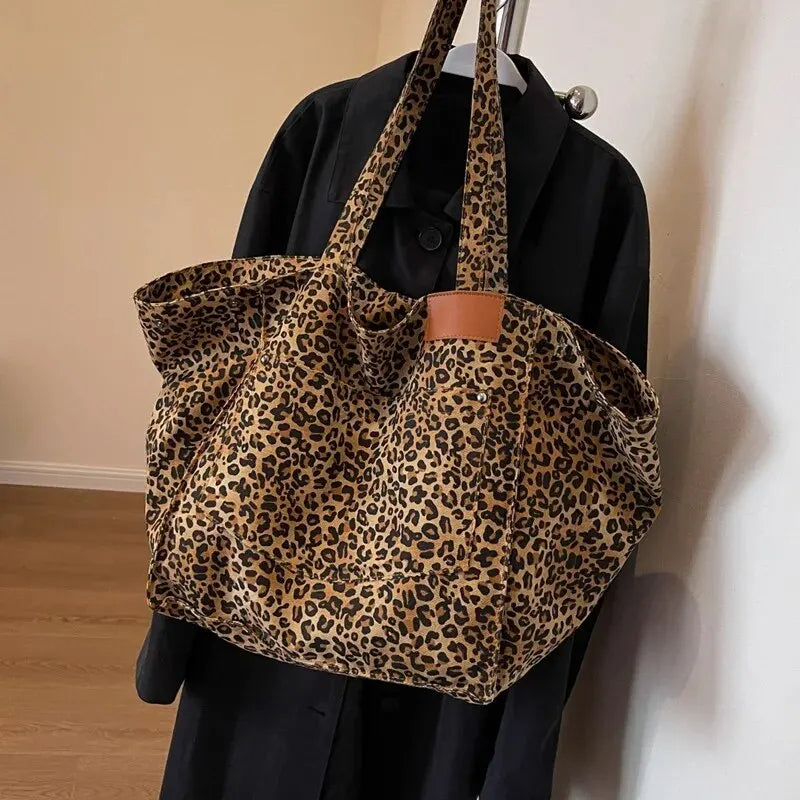 A vintage leopard print canvas tote bag with brown leather trim is displayed hanging on a black garment.