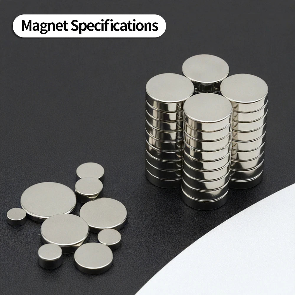 A collection of silver disc magnets stacked and scattered on a dark surface.