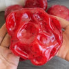 Une main tient un jouet anti-stress en slush de pastèque rouge vif avec des morceaux de fruits visibles.