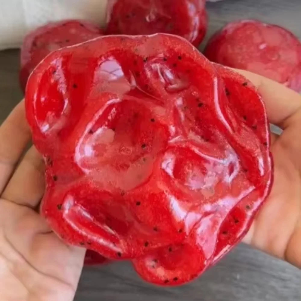 Une main tient un jouet anti-stress en slush de pastèque rouge vif avec des morceaux de fruits visibles.