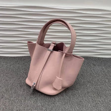 A pale pink classic genuine leather bucket bag with a drawstring closure resting on a gray surface.