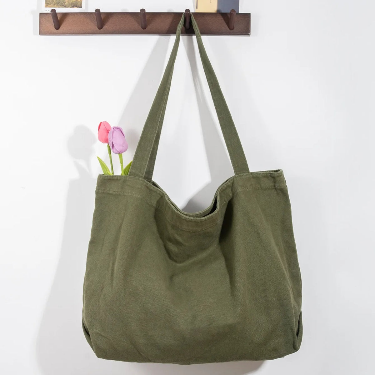 Sac cabas en toile vert olive suspendu contre un mur blanc avec des tulipes roses.