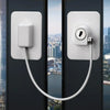 A white window safety lock with two keys is mounted on a dark door frame, featuring a long white cord.