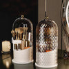 Organizador de vidrio transparente para pinceles de maquillaje y herramientas con tapa giratoria, base blanca.