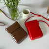 A red vintage PU leather crossbody shoulder bag rests on a white surface next to a glass of green herbs and a white mug.