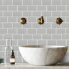 A white marble vessel sink is displayed in front of a gray subway tile backsplash with brass wall hardware.