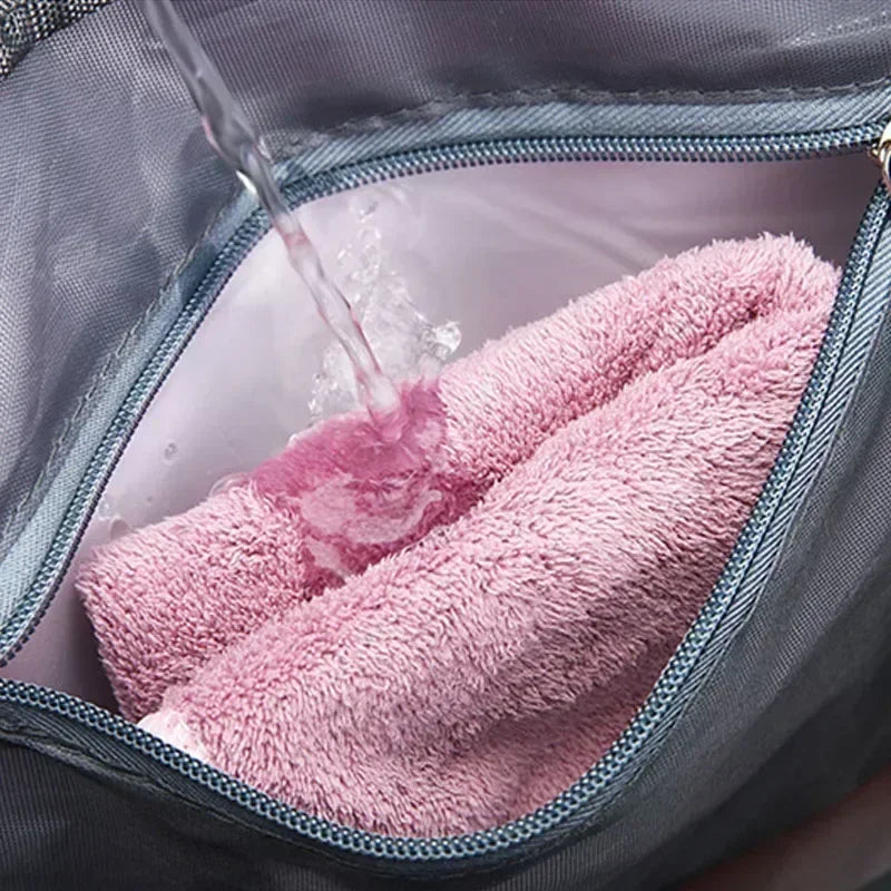 A pink towel is being rinsed inside a gray travel duffel bag with a zipper open.