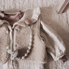 A soft, cream-colored knitted garment featuring a silicone pacifier clip with a teether attached.