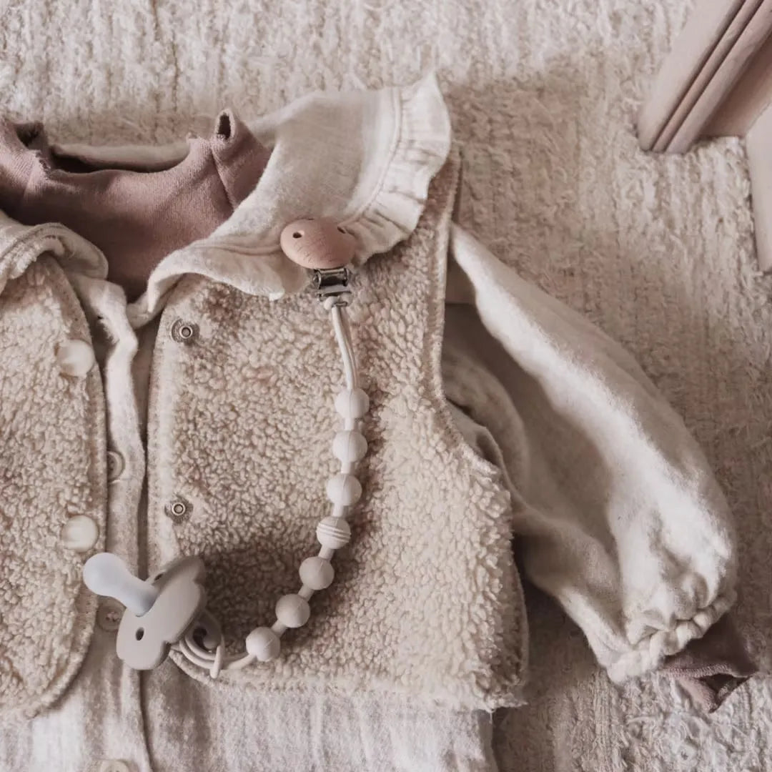 A soft, cream-colored knitted garment featuring a silicone pacifier clip with a teether attached.