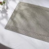 A square linen placemat with embroidered edges is displayed on a white surface.
