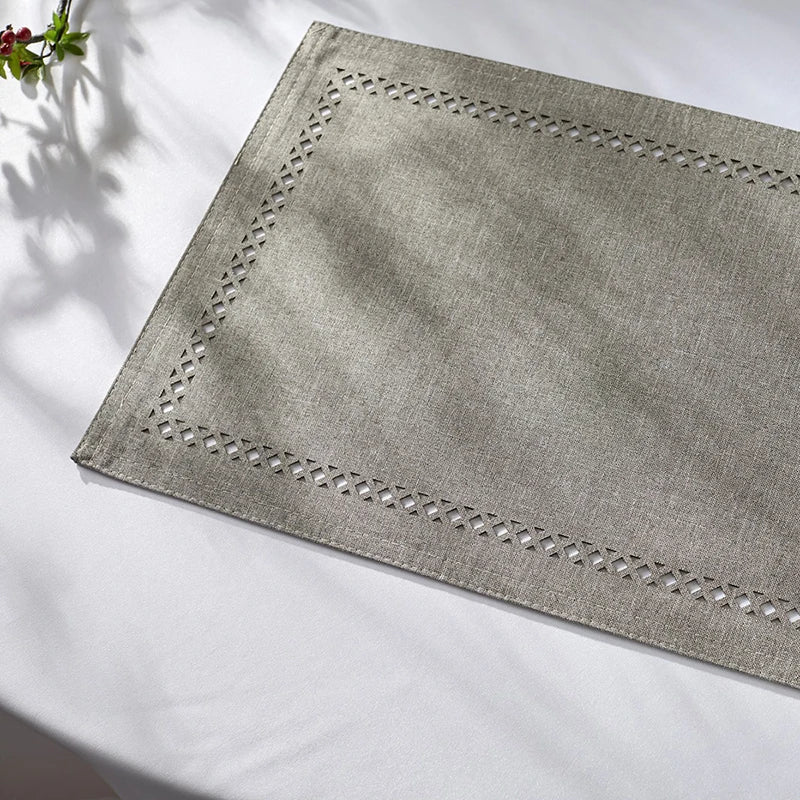 A square linen placemat with embroidered edges is displayed on a white surface.