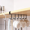 A wooden shelf holds an under-shelf cup and utensil holder with six black hooks for kitchen tools.