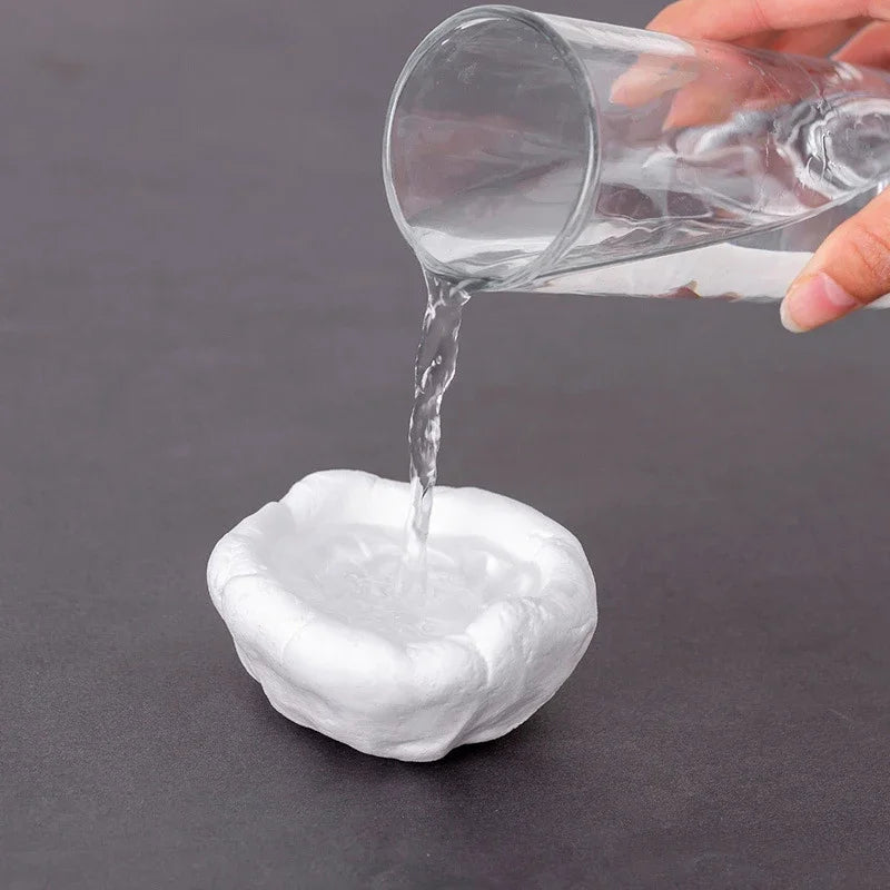 A hand pours clear liquid from a glass into a white moldable sealing clay for AC holes or pipe gaps.