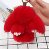 A bright red fluffy angel bunny keychain with a pom pom tail being held by a hand.