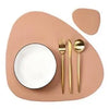 A beige placemat features a white bowl and a gold fork and spoon set.