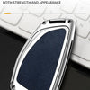 A silver car key case with a dark blue textured insert is shown resting on a white keyboard.