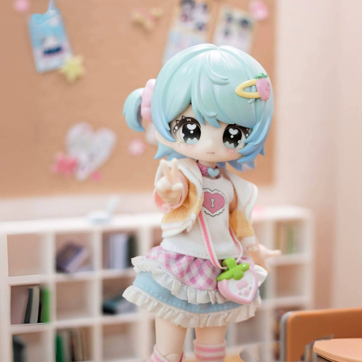 A light blue articulated BJD collectible figurine with pink hair and a white outfit is displayed in a shelf setting.