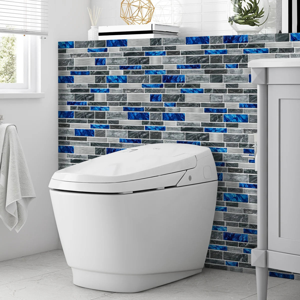 A white toilet is shown in front of a dark blue and gray mosaic tile backsplash.