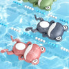 Three wind-up swimming frog bath toys in green, gray, and pink floating in clear blue water.