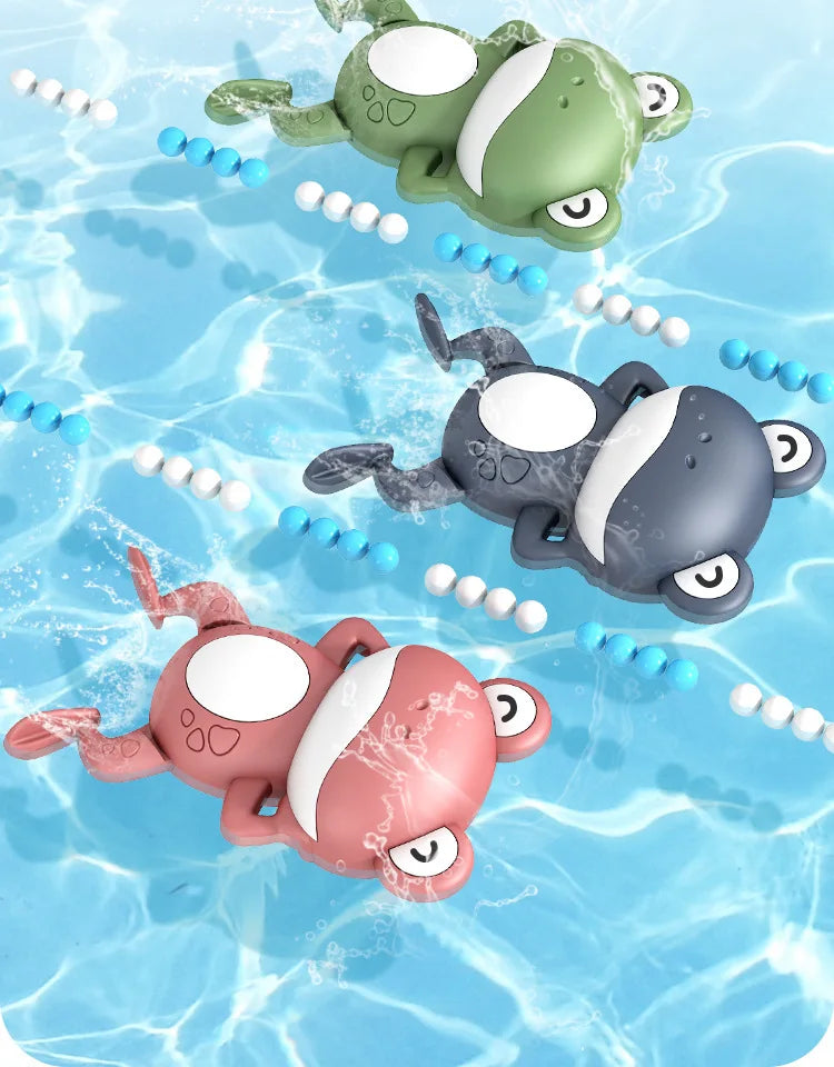 Three wind-up swimming frog bath toys in green, gray, and pink floating in clear blue water.