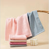A stack of pink, blue, and gray organic cotton face towels hanging on a wooden hanger.