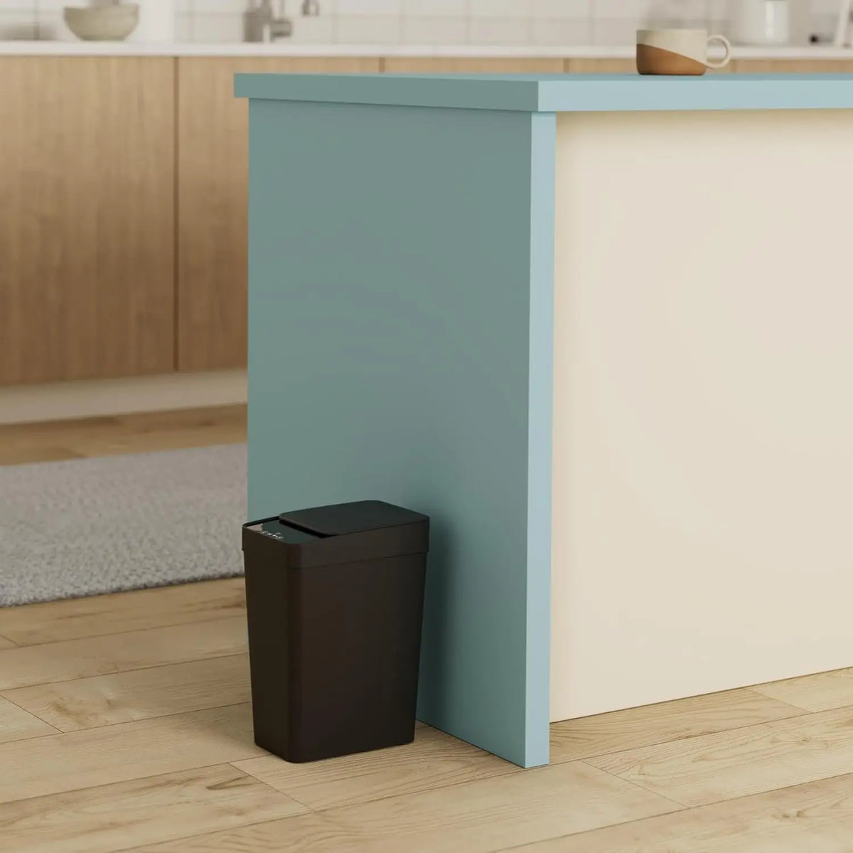 A modern, light blue kitchen island with a cream countertop and a dark trash can placed in front of it.