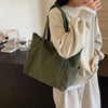 A woman holds a olive green corduroy tote bag with an adjustable strap against a light beige sweater.