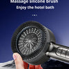 A hand holds a black massage silicone brush shower head against a dark blue background.