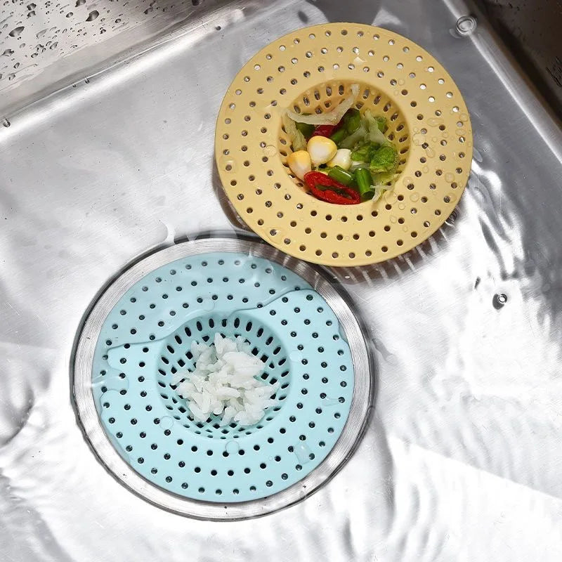 A set of silicone sink drain filters, including a yellow strainer with food, and a blue strainer with chopped garlic.