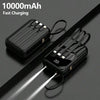 A black 10000mAh portable power bank with built-in cables and a flashlight is shown lying on a dark surface.