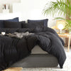 A black duvet cover set with pom-pom trim is displayed on a bed, next to white and gray pillows.