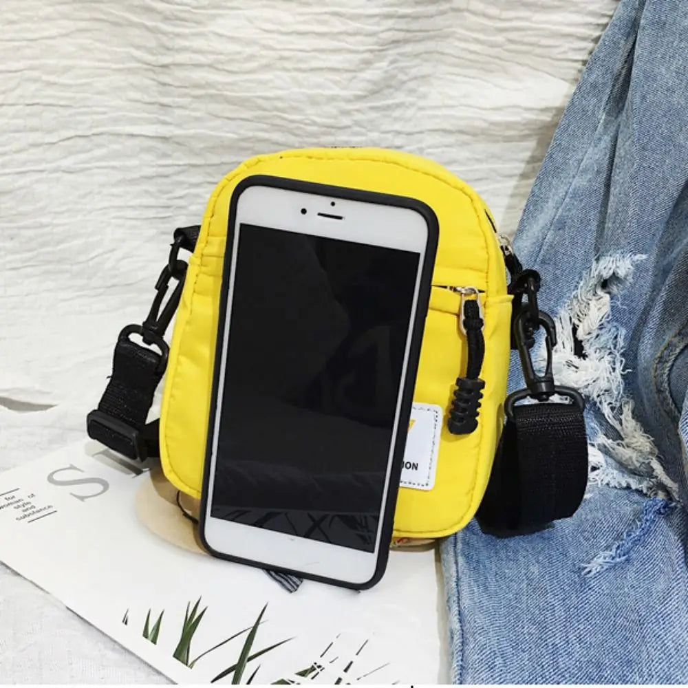 A yellow mini canvas crossbody bag with a black smartphone attached, resting on a denim fabric.