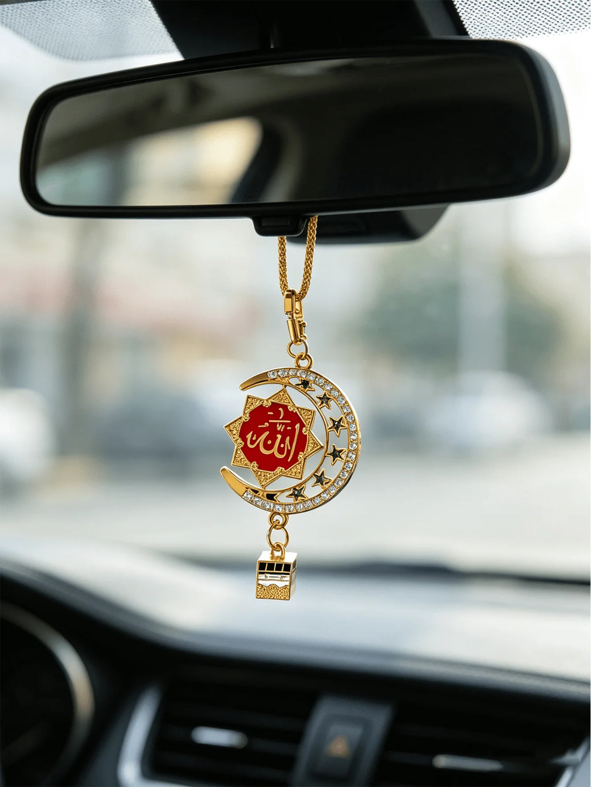 Gold-tone Islamic calligraphy pendant with a star and crescent design hanging from a chain, displayed in a car mirror.