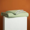 A light green cooling summer blanket folded on a white pedestal against an orange background.