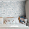 A bedroom wall decorated with a white wallpaper featuring delicate blue botanical and star patterns.