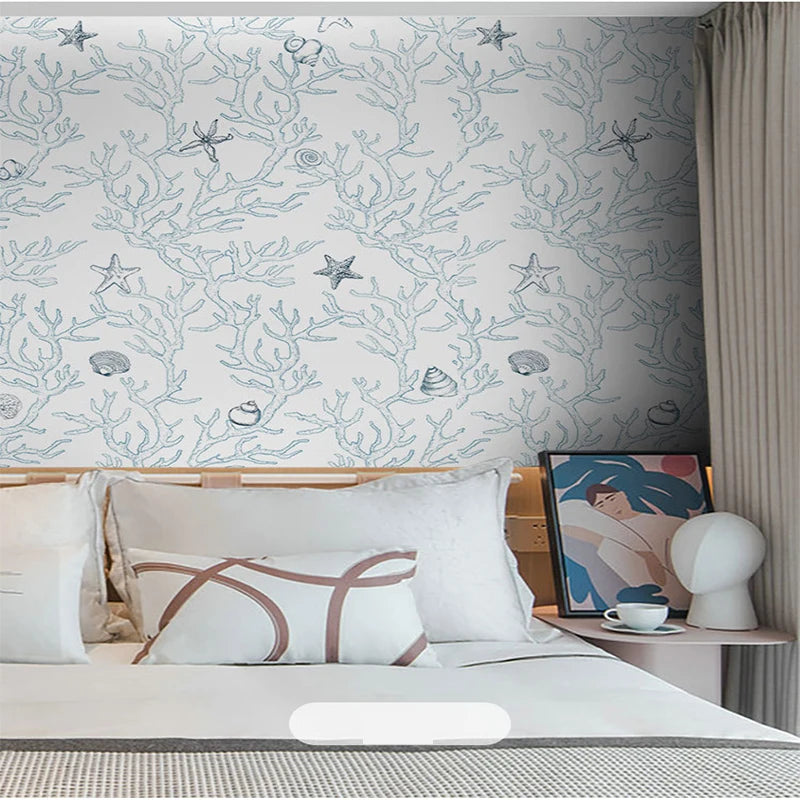 A bedroom wall decorated with a white wallpaper featuring delicate blue botanical and star patterns.