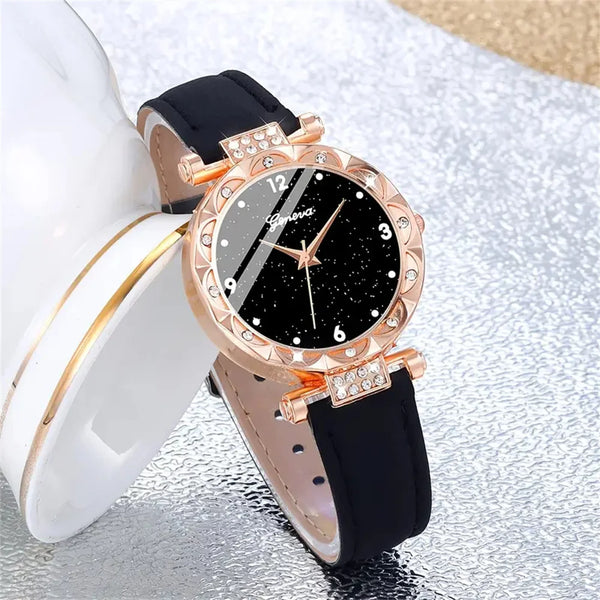 A close-up of an elegant rhinestone quartz watch with a gold-toned case and black leather band resting on a silver surface.