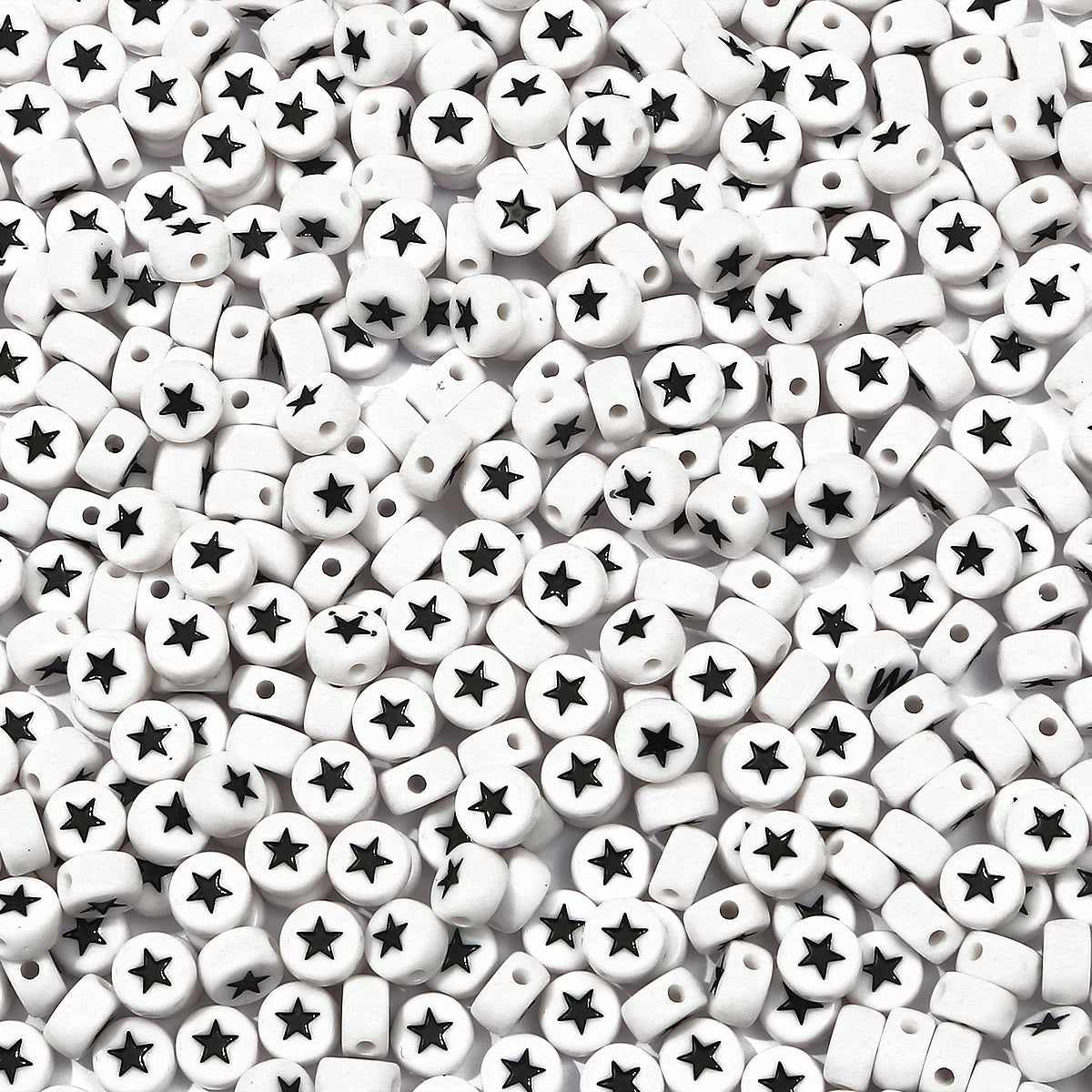 A close-up view of small white and black acrylic letter beads scattered on a white surface.