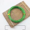 Green anodized aluminum jewelry wire coiled on a wooden board with twine.