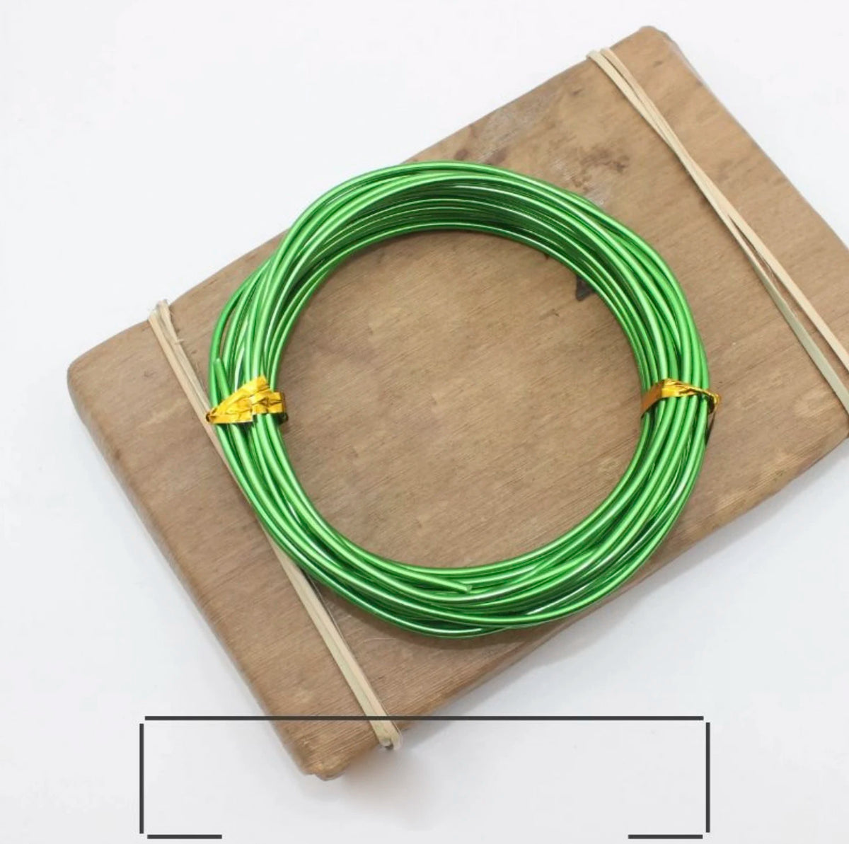 Green anodized aluminum jewelry wire coiled on a wooden board with twine.