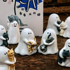 A collection of white ghost-like figurines, some holding cats and other small animals, displayed in front of a box with Chine