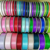 A stack of double face satin ribbon in various solid colors, including pink, teal, purple, and green.