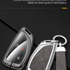A black key case with a silver metal key and a dark gray leather strap is shown on a black background.