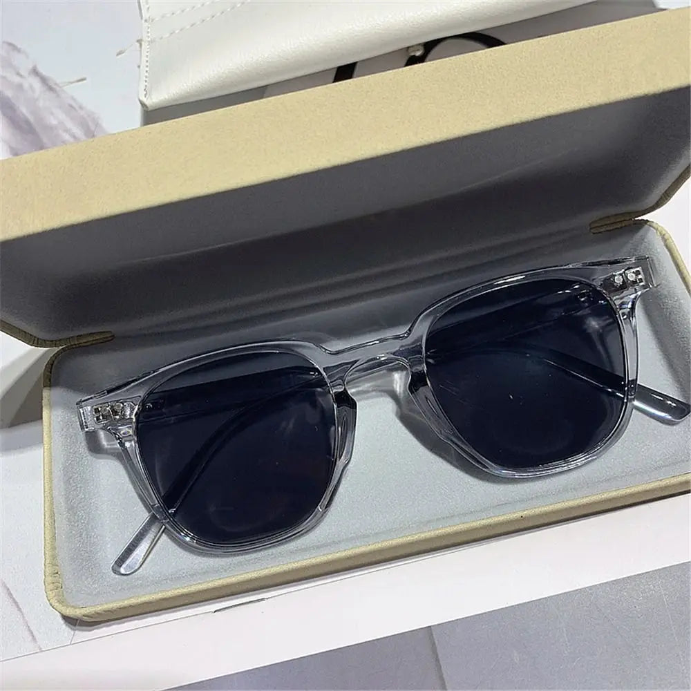 A pair of vintage square sunglasses with clear frames and dark lenses resting in a light-colored box.
