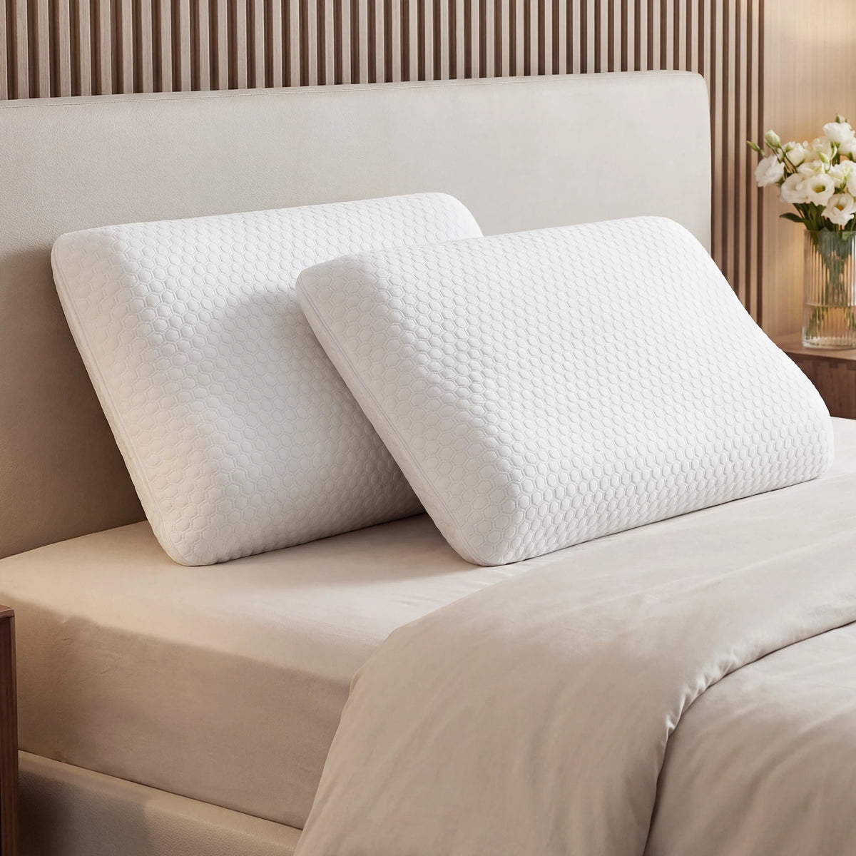 Two white memory foam pillows with a quilted texture resting on a beige bed with wooden paneling.