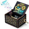 A vintage hand-cranked wooden music box with a lid open, featuring a sunflower design and musical notes.