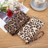 A pair of leopard print retro long wallet for women resting on a wooden table next to a cup and some flowers.