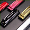 A collection of harmonica products including a red and silver harmonica in a case and several black diatonic harmonicas.
